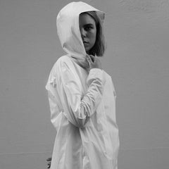 Model wearing the white rain jacket with pockets and hood. The stylish parka has buttons running along the front of the jacket. cruba
